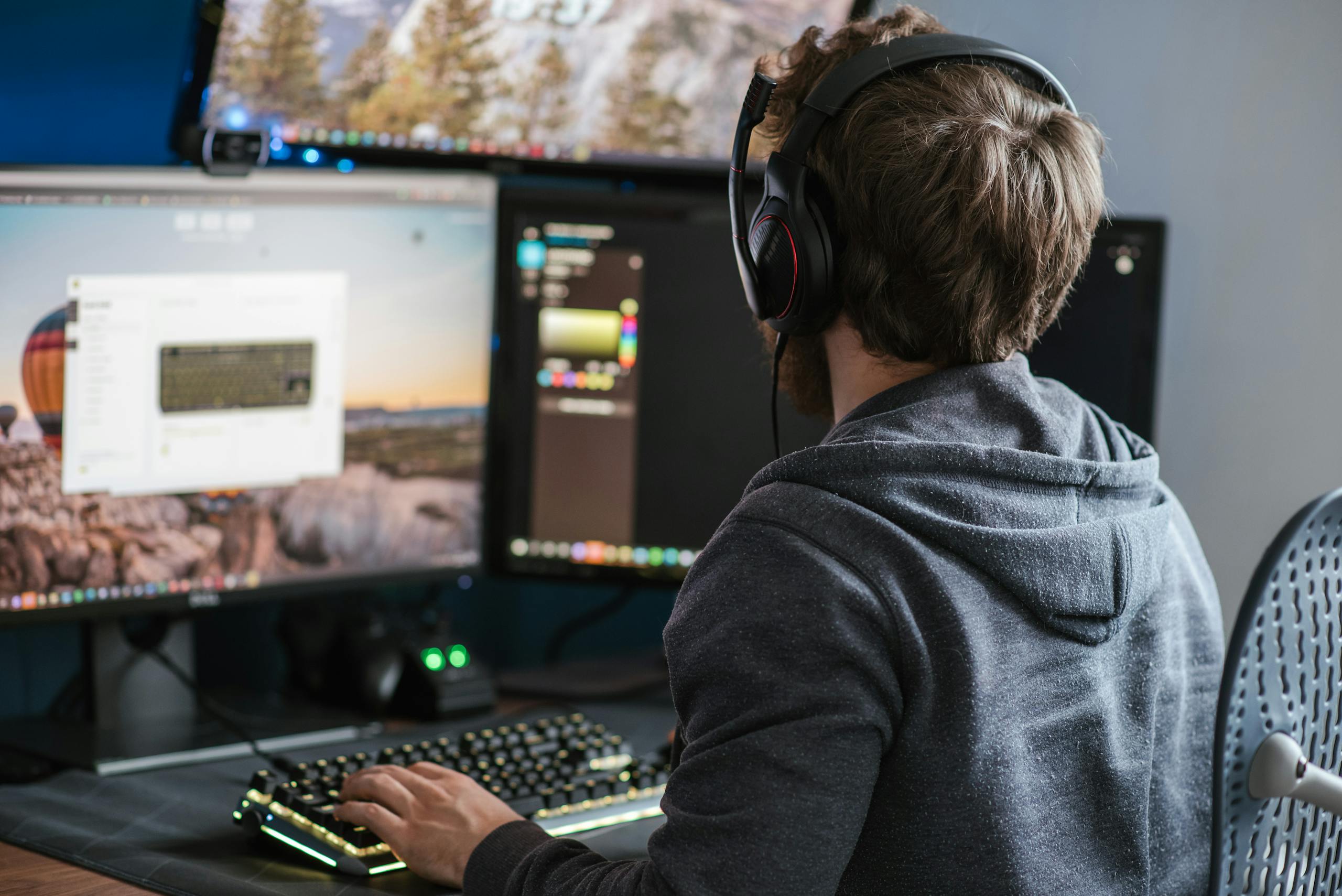 Adult man in casual attire working on dual monitors, wearing headphones, indoors.